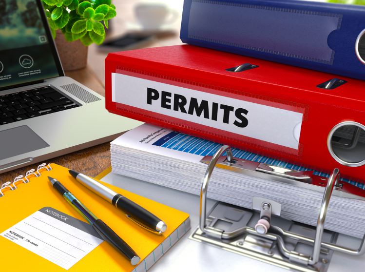 Opening a Gas Station: From a $1M Startup to $37M/Year 3 Binders of business information about permits and licenses stacked on a desk next to a laptop.