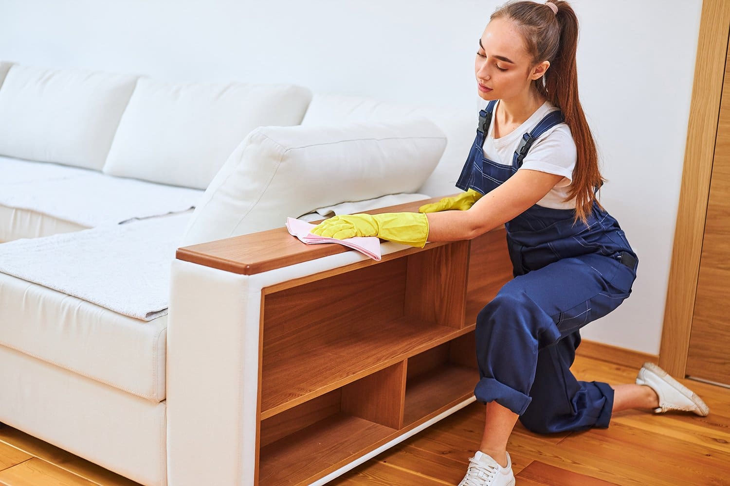 Youthful woman wearing blue uniform wiping dust off the sofa