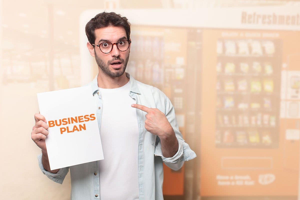 Business owner standing in front of vending machines and pointing to business plan document