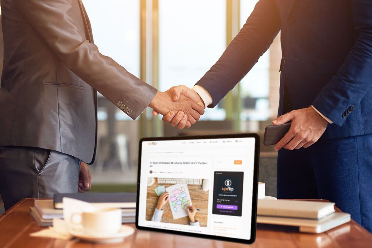 Business people shaking hands over a desk with books, coffee cup, and tablet