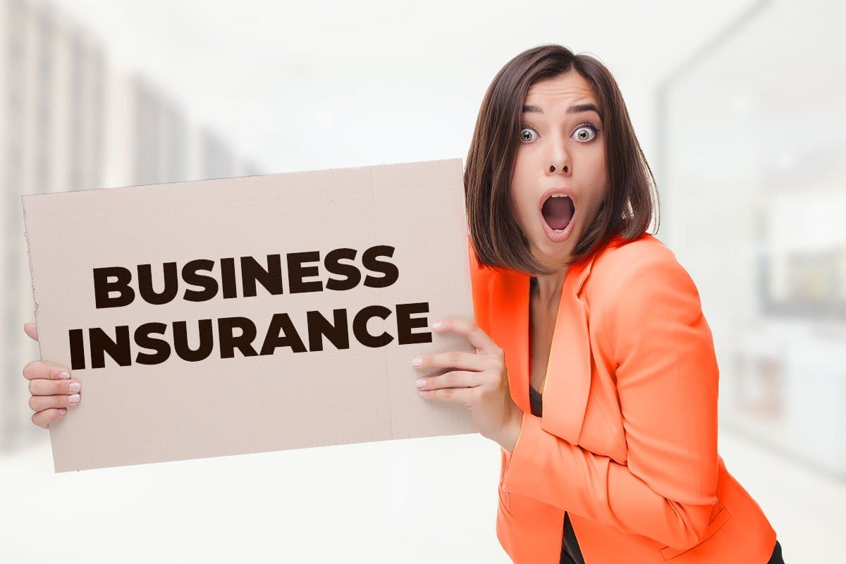 Startled woman business owner holding sign with words "business insurance" in all caps