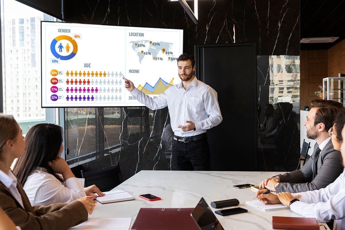 Business person presenting slide on demographics to others in a board room