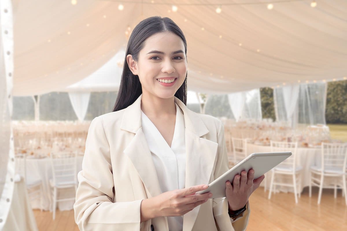 Woman event planner holding a tablet under a beautifully decorated white wedding tent