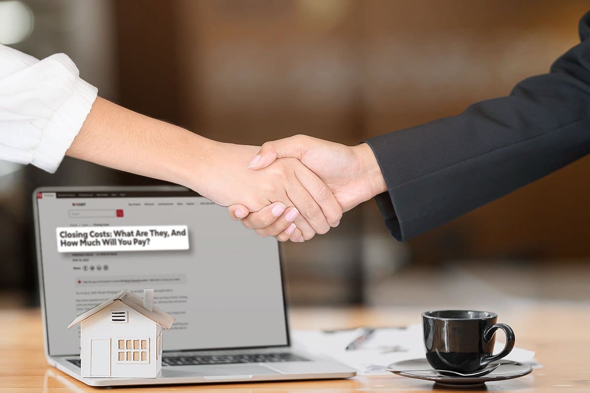Business person and buyer shaking hands over a laptop, miniature house, and cup of coffee