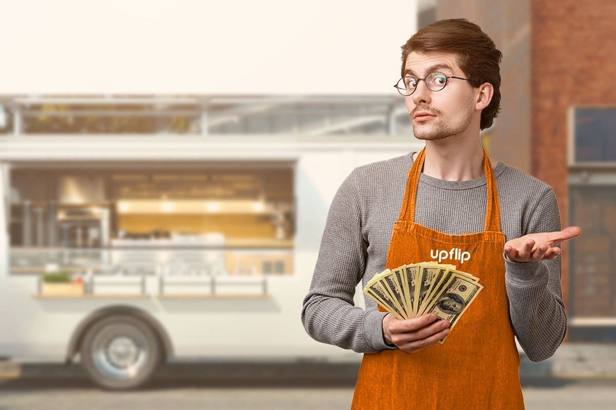 Man in an orange UpFlip apron standing in front of a food truck and holding cash