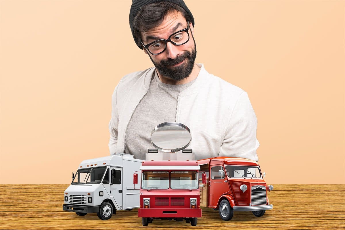 Concept of bearded man in a beanie and glasses looking at model food trucks with a magnifying glass