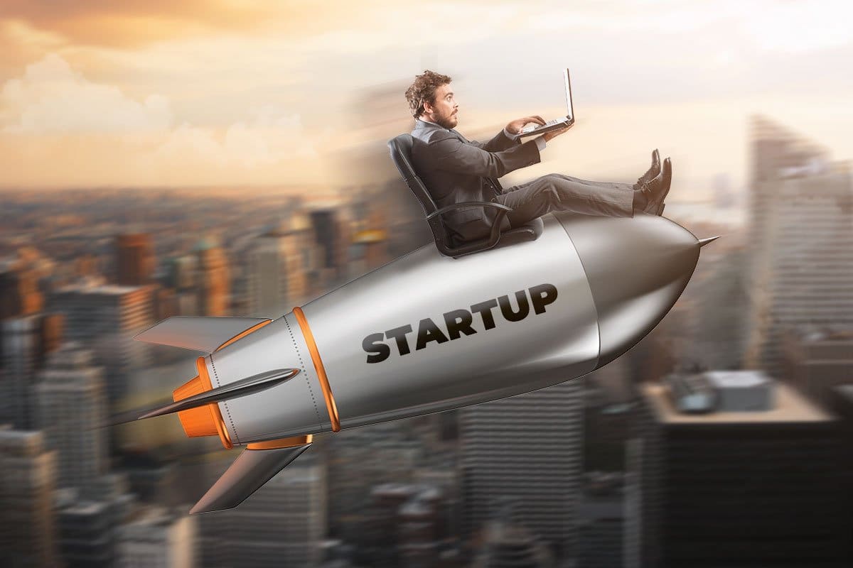 Concept of entrepreneur riding a small rocket with the word "startup" on the side over a cityscape