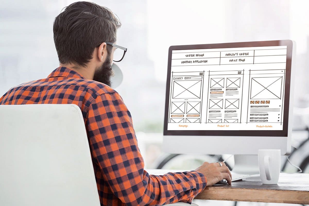 Cleaning Business Website 7-Step Guide 1 Web designer in a plaid button-down shirt working at a desktop computer