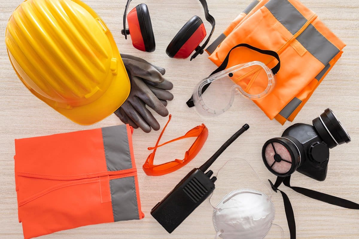 23 eCommerce Business Ideas You Can Start Today 12 Top-down shot of PPE ideas for ecommerce business including hard hat, gloves, masks, goggles, and reflective vest arranged on a wood grain table