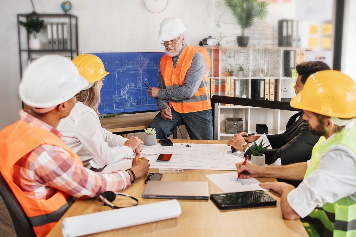 Construction company target market training with participants in a board room and instructor pointing to new home blueprint