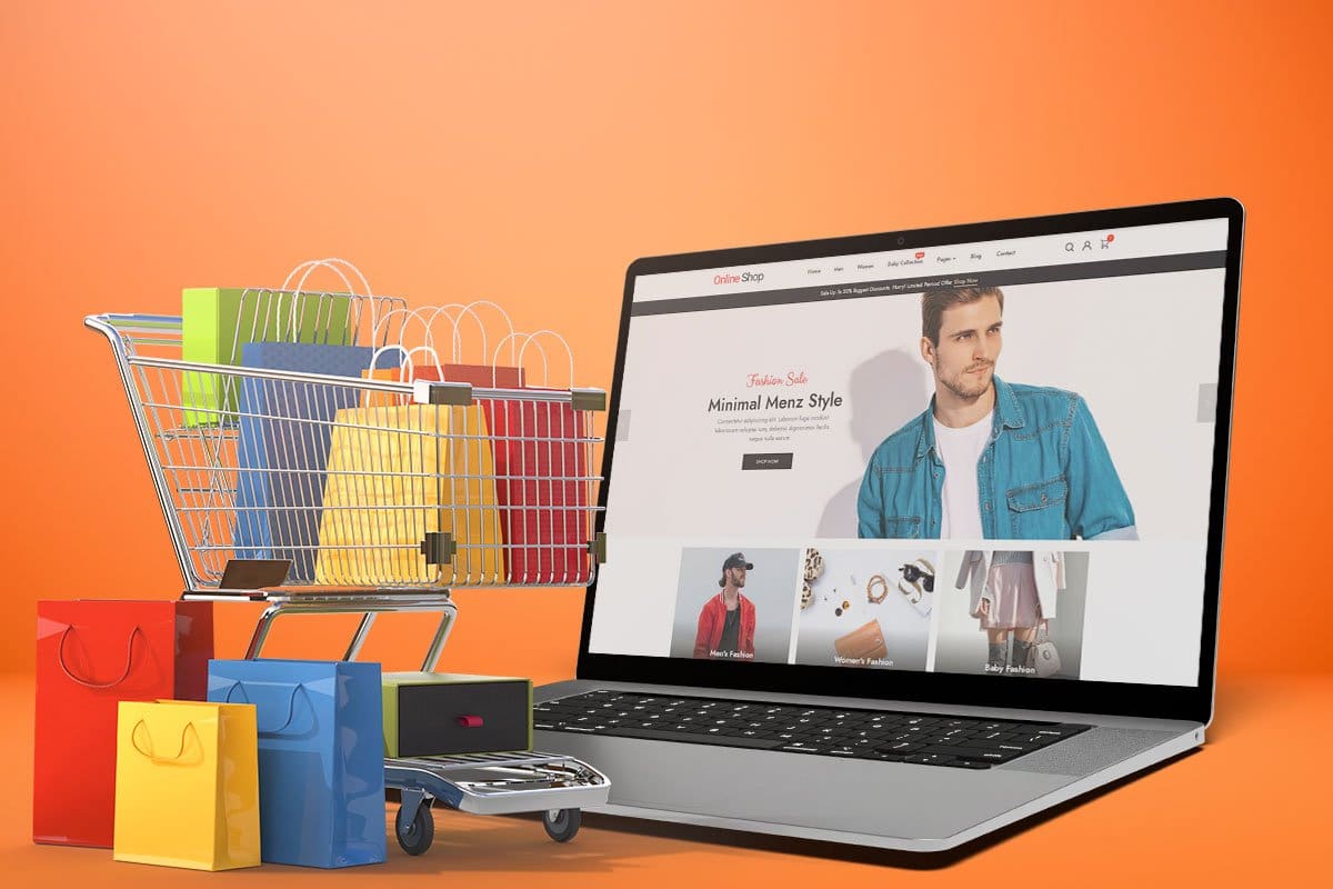 Concept showing a men’s fashion website loaded on a laptop next to a miniature shopping cart loaded with and surrounded by brightly colored shopping bags