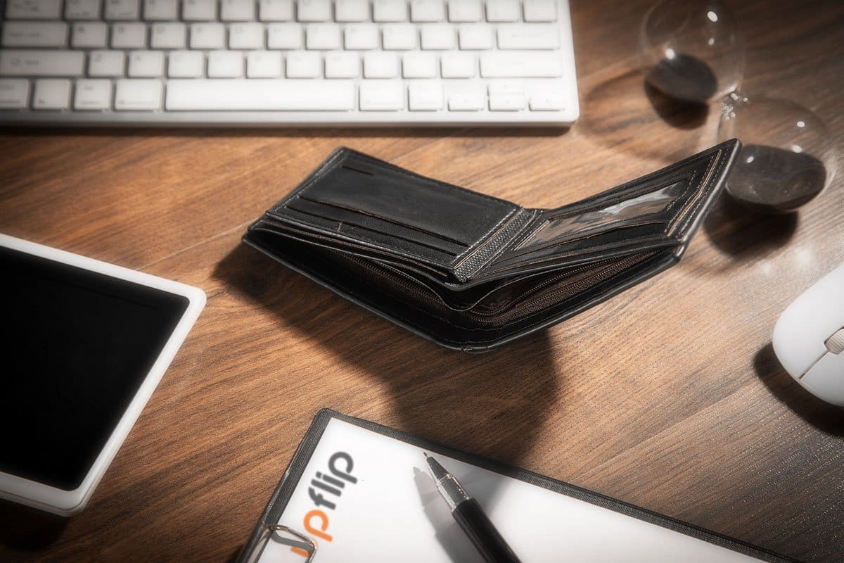 Empty wallet on a wood grain desk next to a mouse, keyboard, and tablet