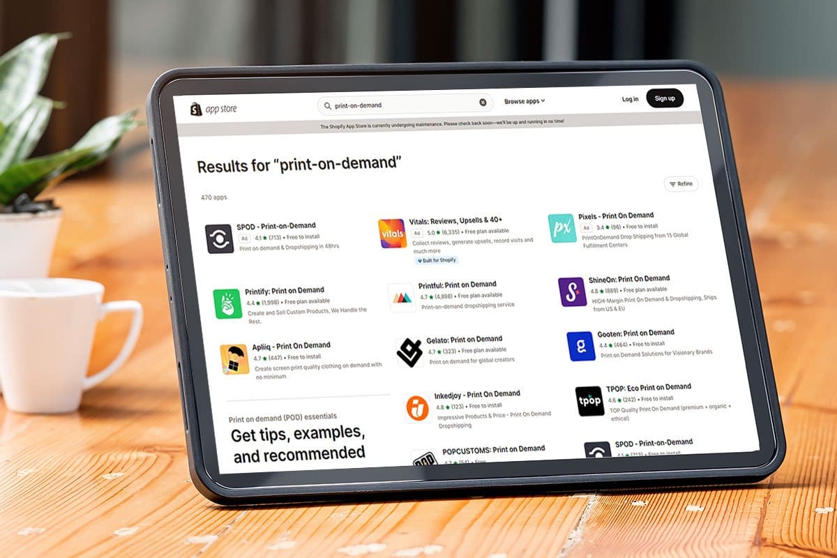 The 11 Best Print-on-Demand Companies of 2025 13 Shopify "print-on-demand" app options loaded on a tablet next to a potted plant and a cup of coffee