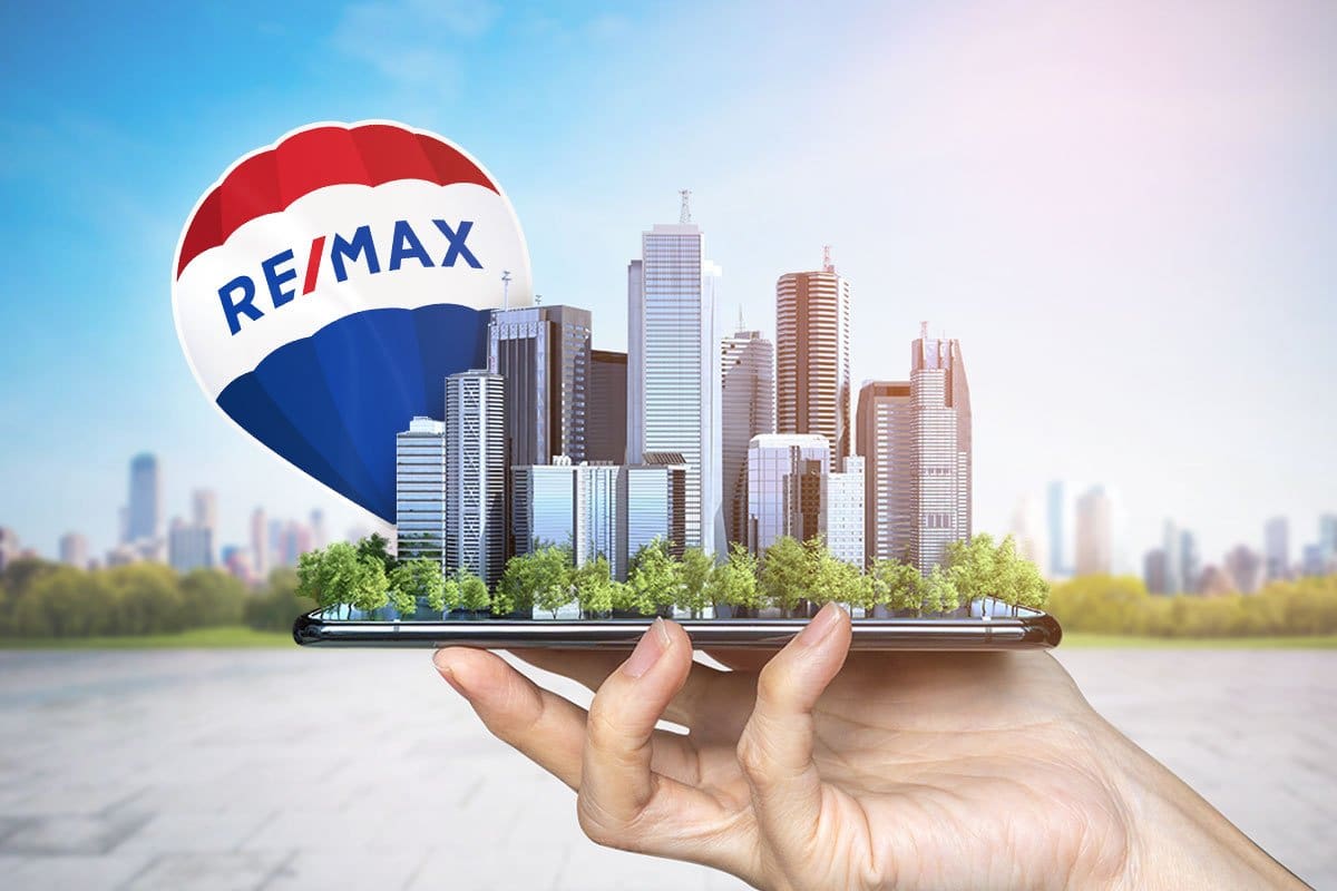 RE/MAX realty concept showing a cityscape and a red, white, and blue RE/MAX hot air balloon "growing" out of a smartphone held in a woman’s hand