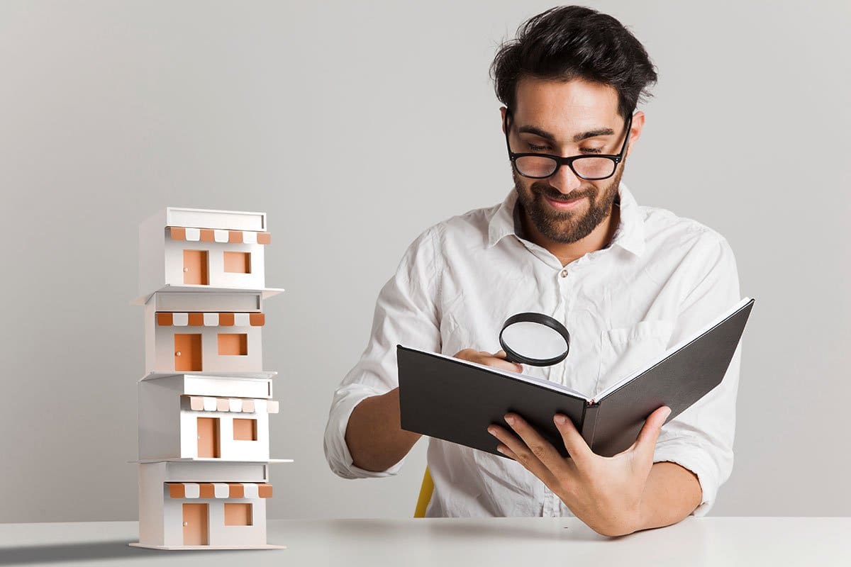 The 11 Best Print-on-Demand Companies of 2025 6 Casually dressed man looking over documents with a magnifying glass and miniature model storefronts stacked up on the table he’s sitting at