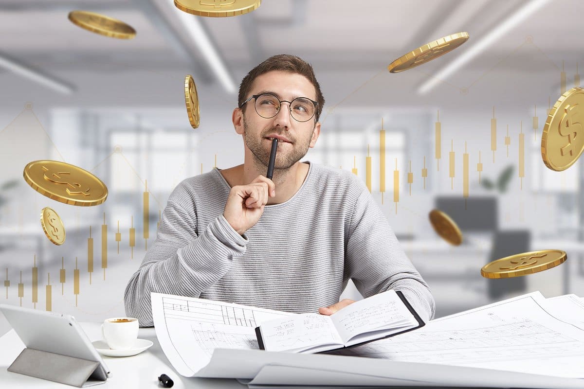 Man in glasses and a casual sweater sitting at a desk reviewing financial paperwork with coins flying overhead