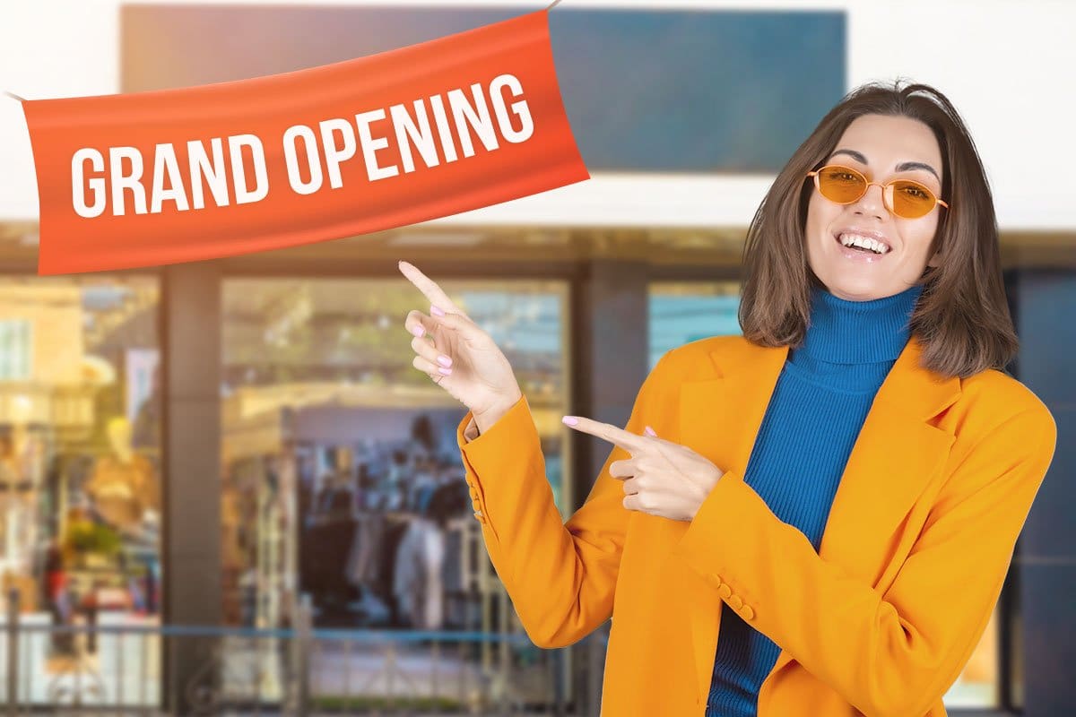 276 Boutique Names (for 2025) 8 Smartly dressed woman pointing to a grand opening sign hung outside a new boutique