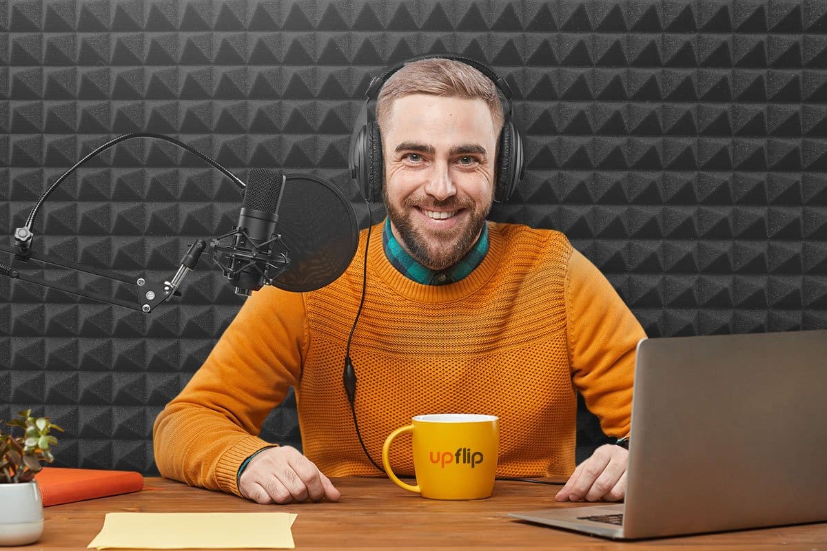 How to Grow a Podcast (2025) 1 Middle aged man podcaster in an orange sweater with an orange UpFlip mug in a recording booth