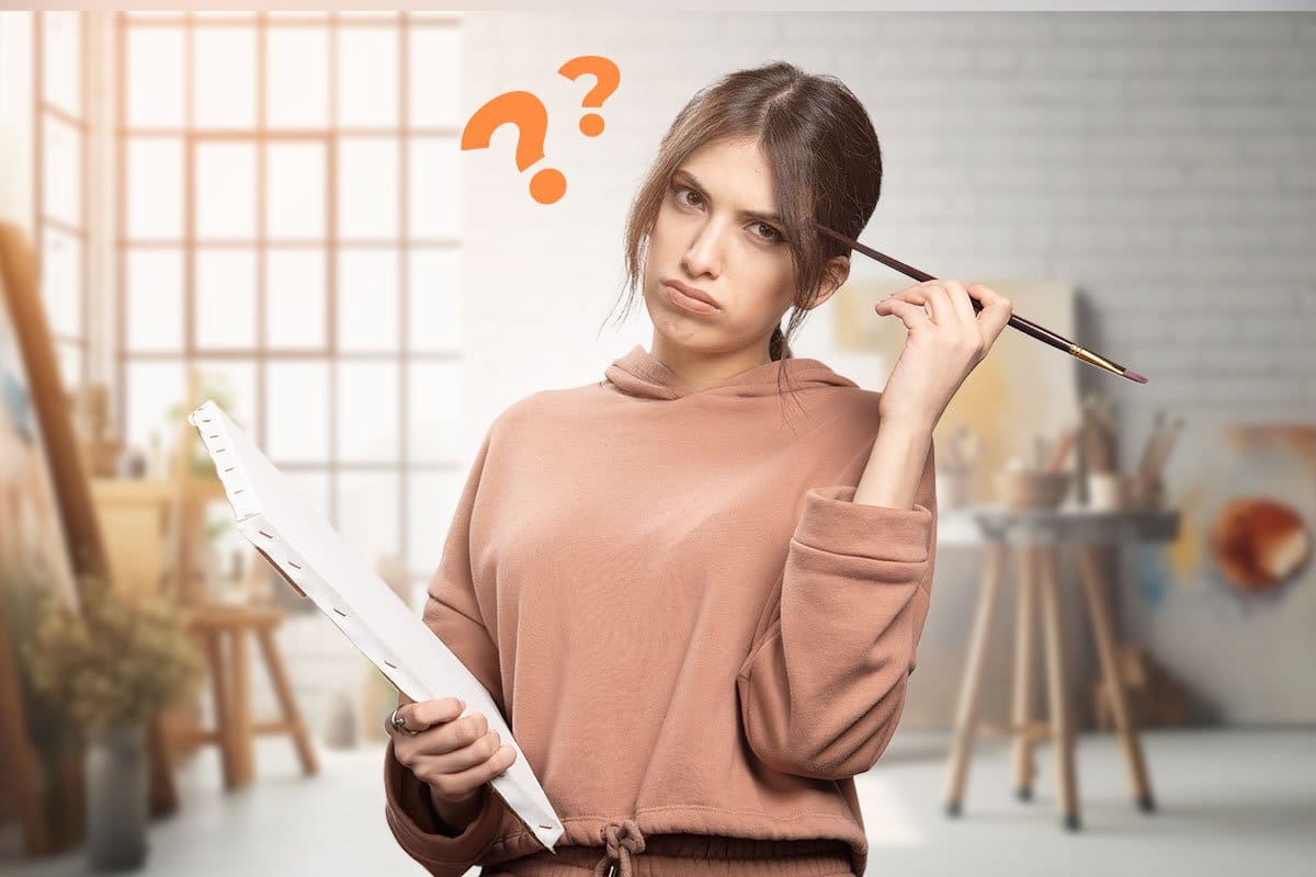 Artist with a thinking face in her studio holding a paint brush and a canvas with two question marks hovering overhead