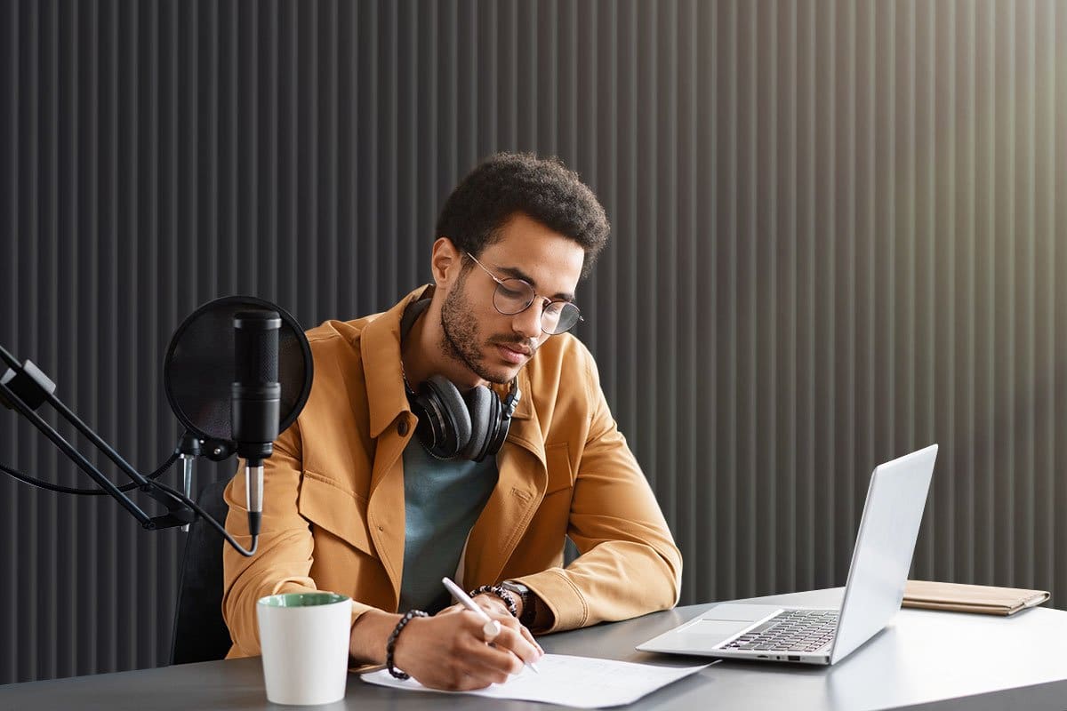 How to Grow a Podcast (2025) 2 Young man podcaster taking notes in a sound booth