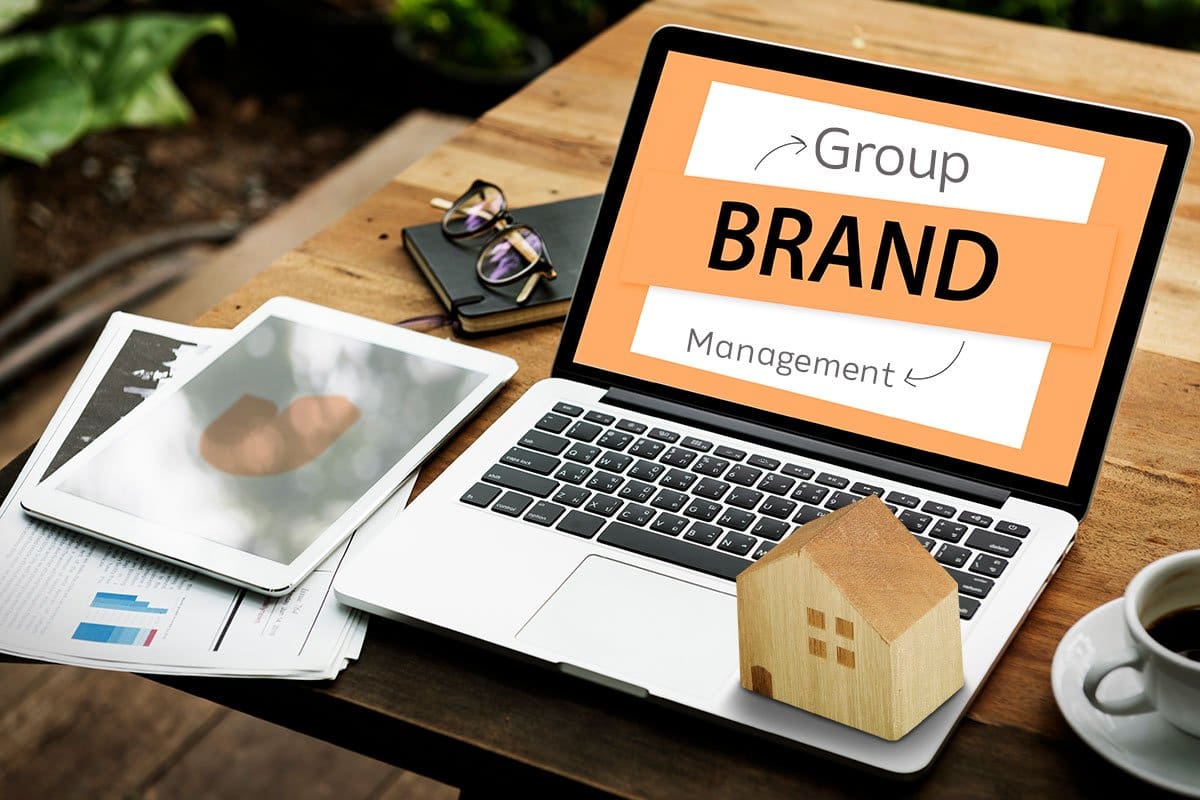 Branding brainstorming session with laptop, tablet, coffee, printed reports, and a miniature wooden house on an outdoor table