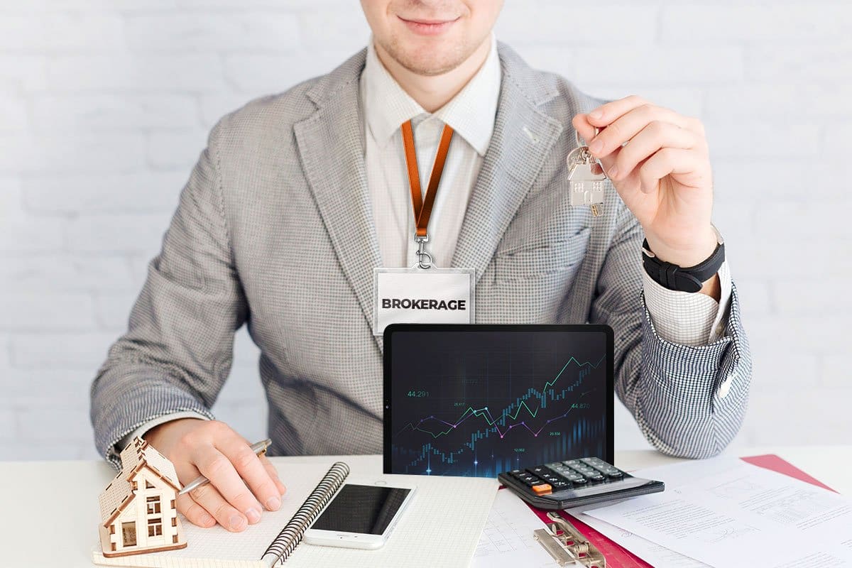 Broker sitting across a table from the camera preparing for a meeting with a notepad, calculator, tablet, documents, and keys