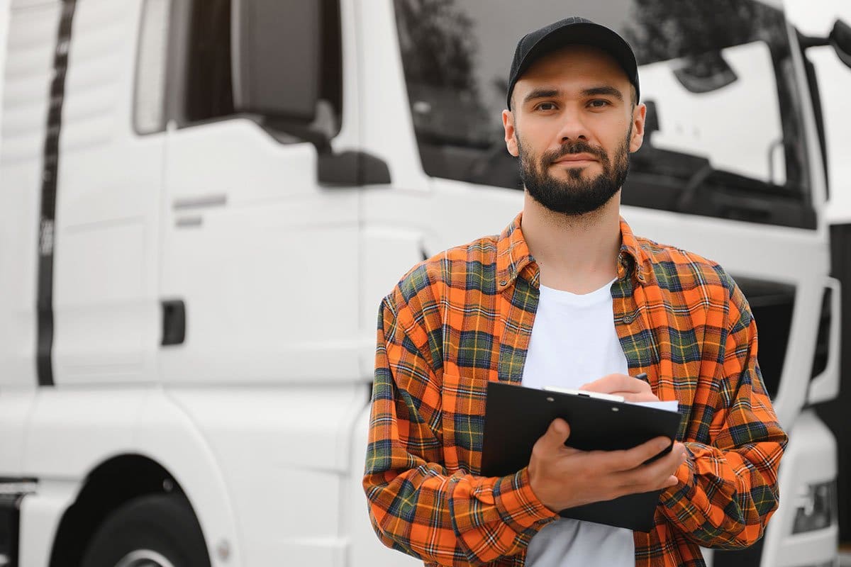 200 Trucking Company Names for 2025 2 Trucker in an orange plaid button down shirt standing in front of a white box truck taking notes on a clipboard