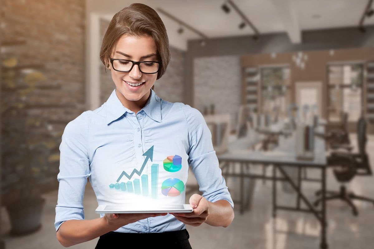 Concept of woman working on tablet with upward trending graph and pie chart holographs hovering above the screen to show what she’s working on