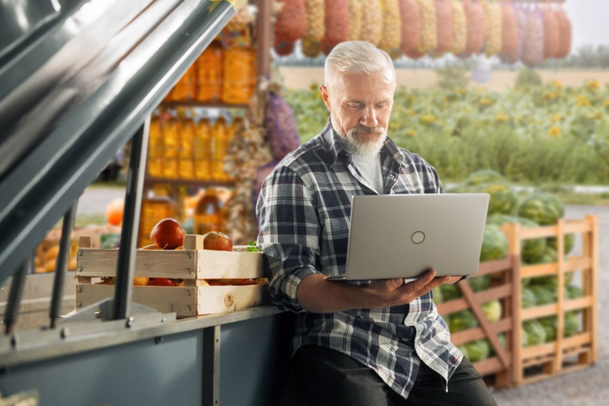 How to Start a Farm (and Make $120K/Month) in 2025 3 Farmer leaning on a farm stand with apples and other produce using a laptop