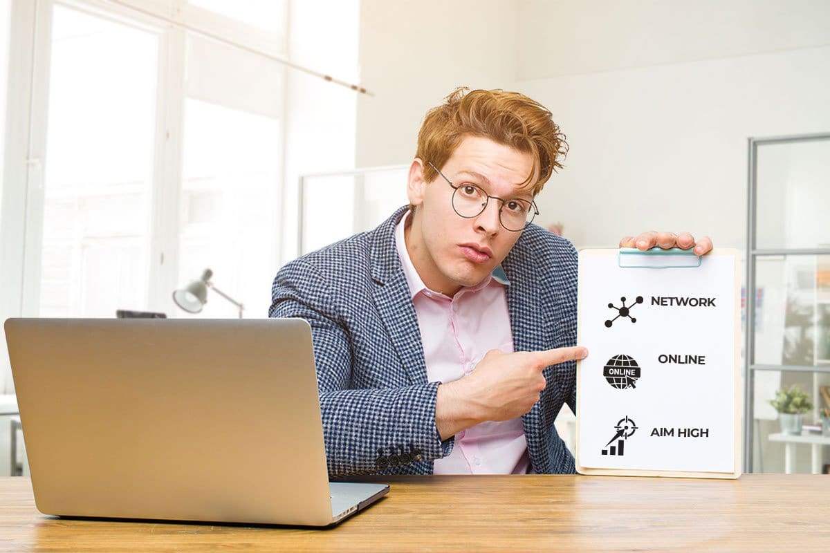 Man at a laptop pointing to a clipboard with masterminding tips that read "network", "online", and "aim high"