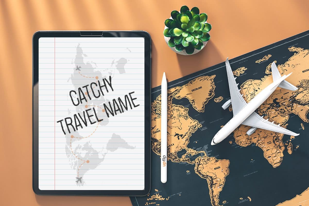 338 Eye-Catching Travel Agency Names 1 Top-down shot of a travel agent’s desk with a succulent, a miniature airplane, a black and orange map of the world, and a tablet with the words "catchy travel name" on it