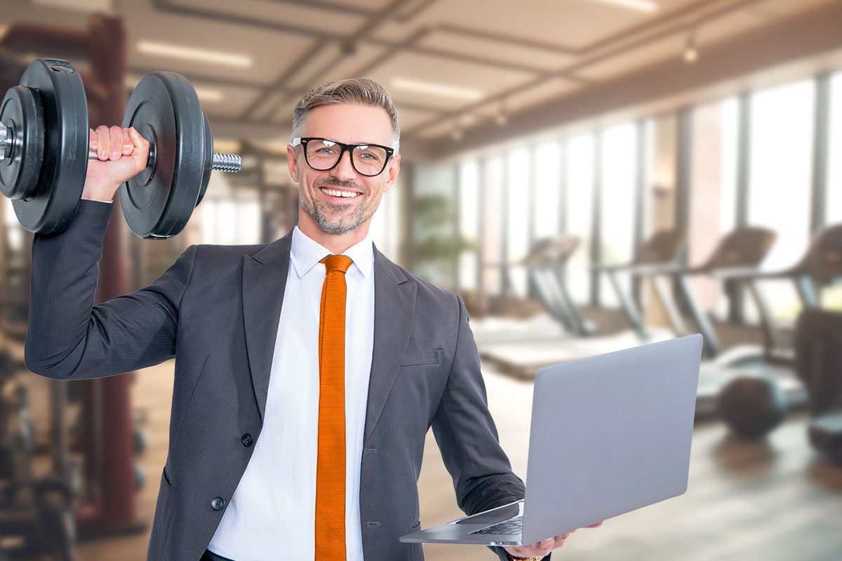 Businessman in a suit with a laptop in one hand and a dumbbell in the other.