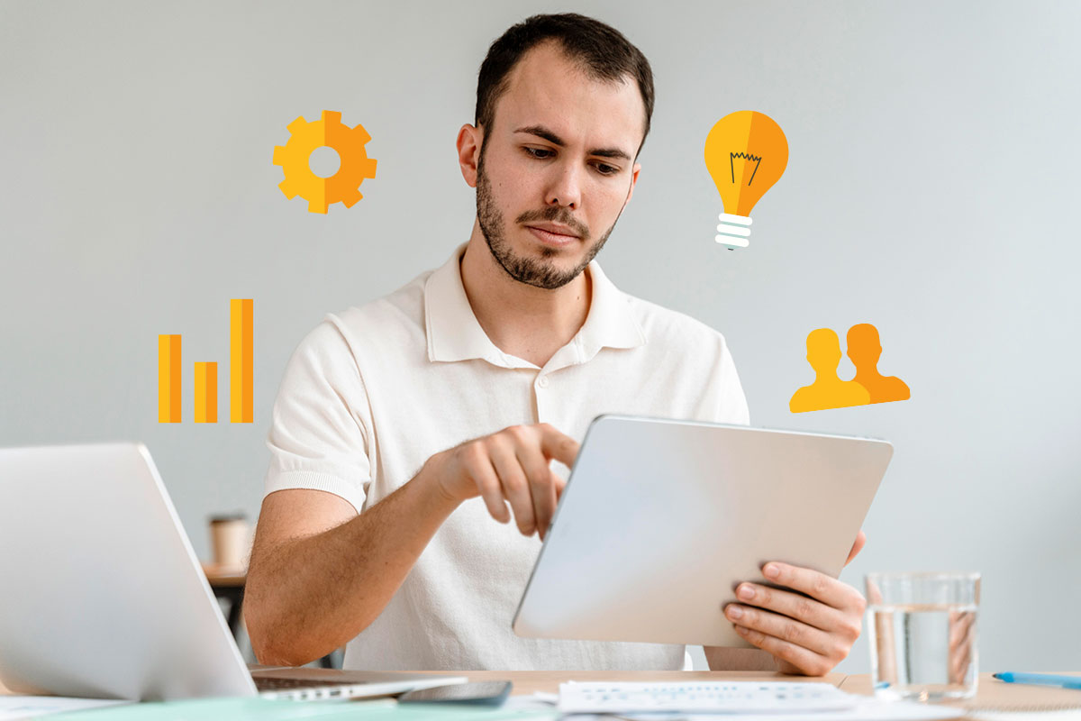 Man working on a tablet with a graph, gear, lightbulb, and networking icons hovering around him.