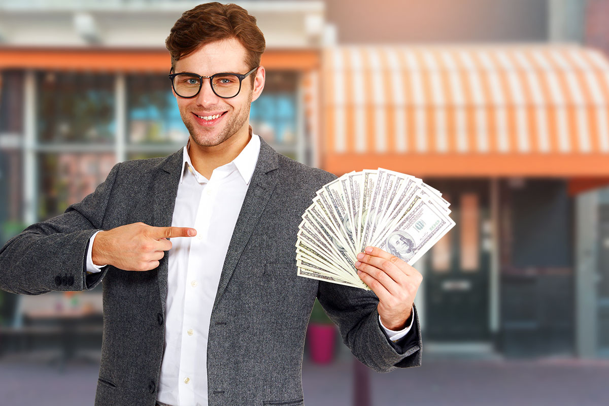 Turnkey Business: The Ultimate Guide (2025) 7 Smiling man in a sport coat holding and pointing to a fan of cash