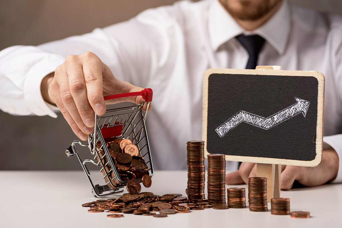 Man in a button down and tie dumping coins from a miniature shopping cart onto a counter