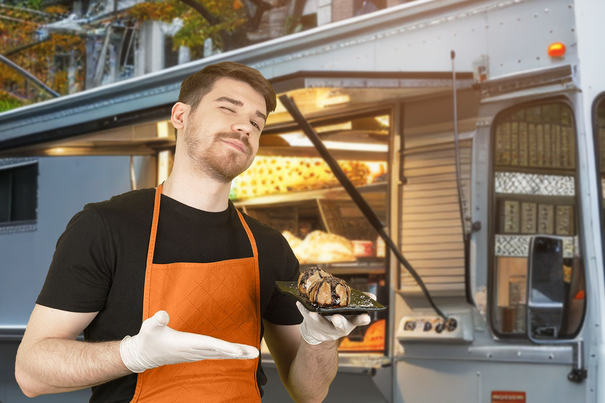 Food truck owner standing by truck and gesturing to a sample of baked desserts