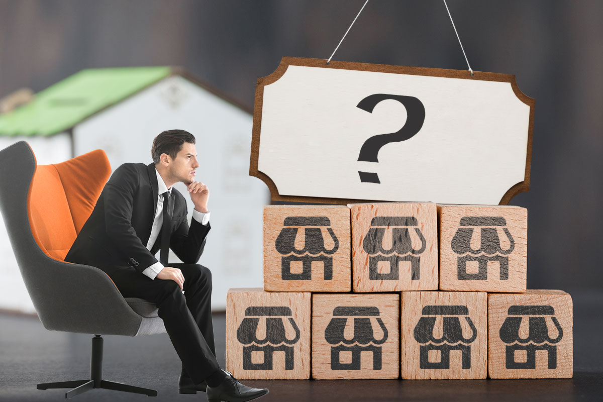 Businessman sitting on a chair looking at wooden blocks with storefront symbols