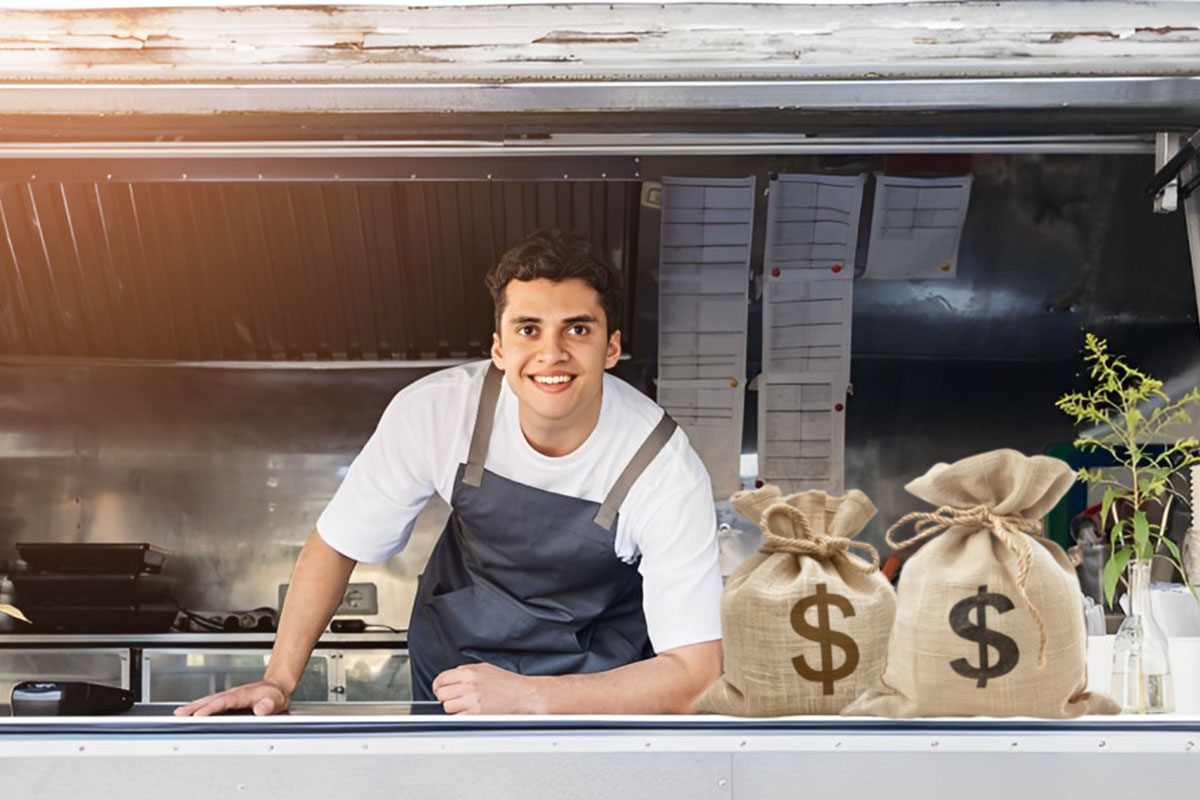 Business owner posing in window of a food truck next to bags of money