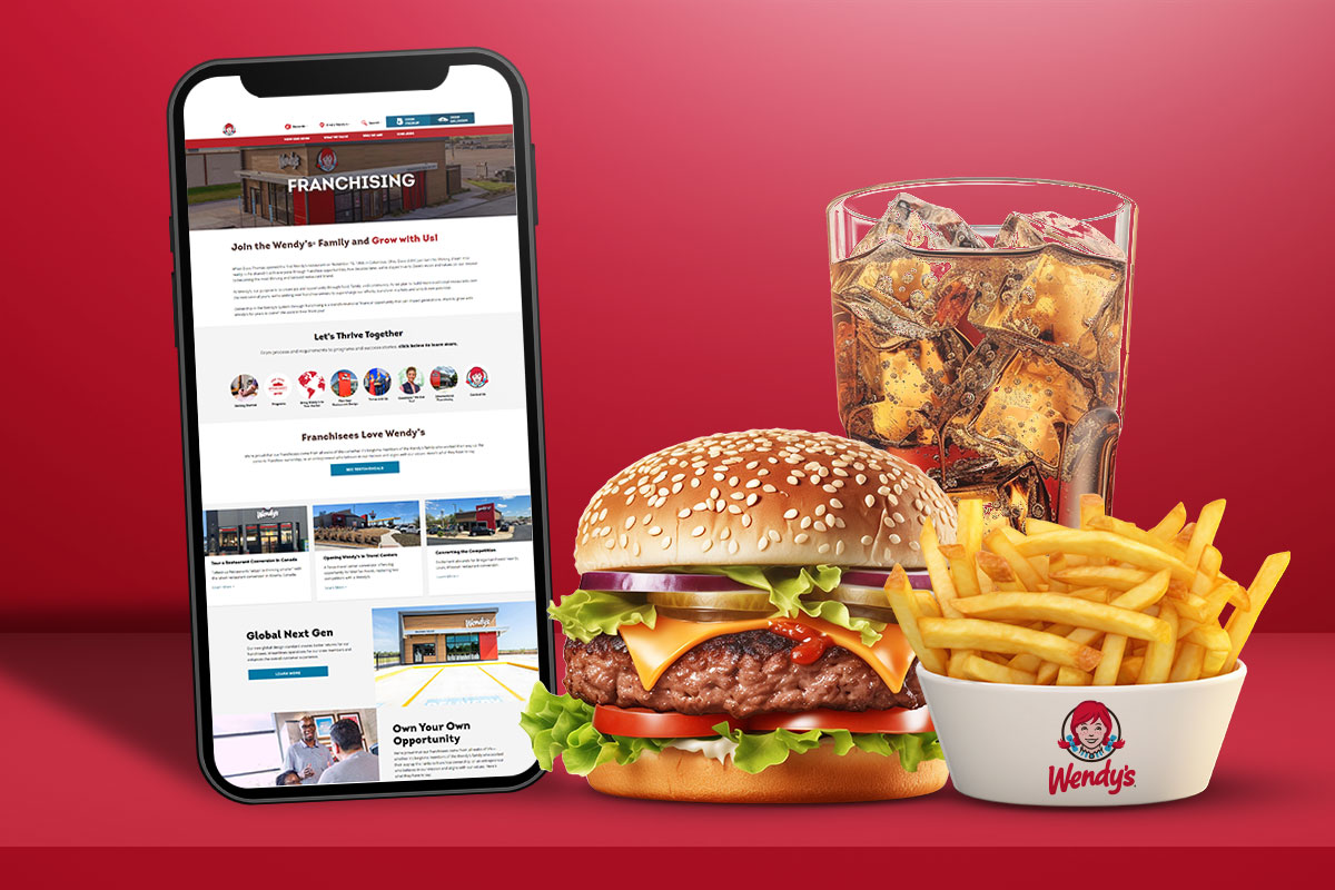 A cell phone open to a Wendy's franchising page next to a cheeseburger, fries, and soda from Wendy's