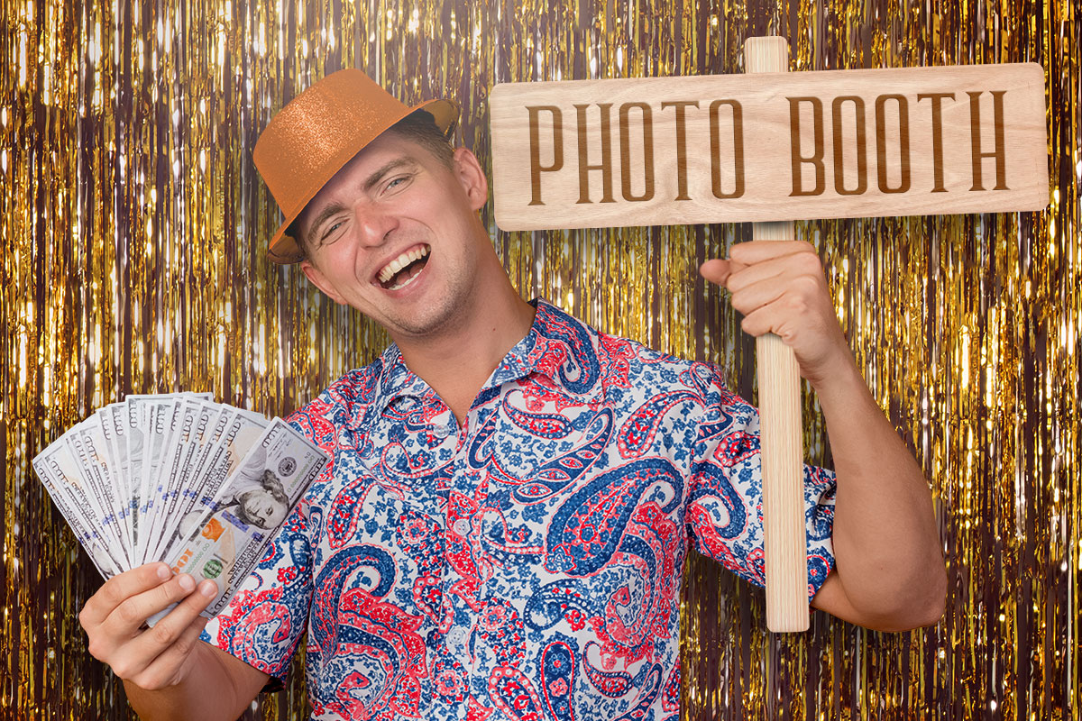 Photo booth owner holding cash and using photo booth props in front of a gold background