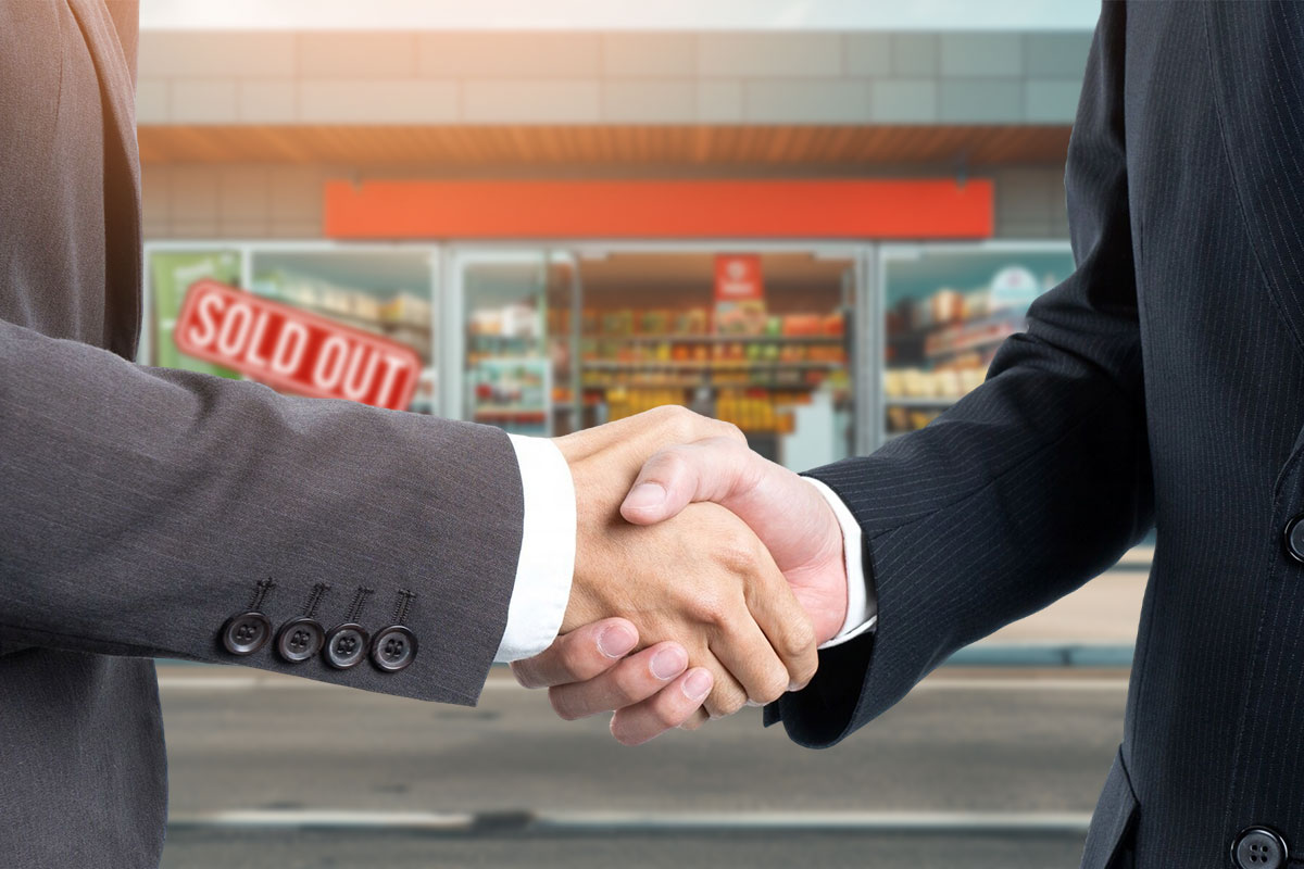 Two people in suits shaking hands outside of a convenience store with a sign that says "sold out"