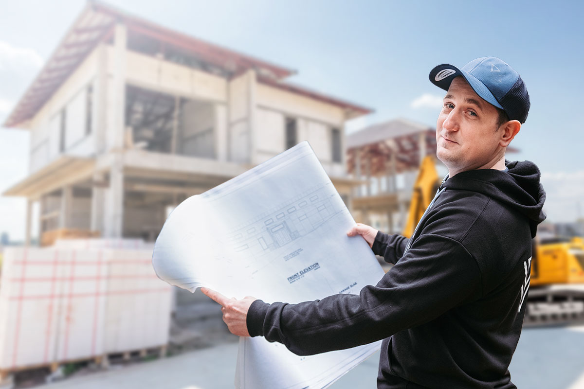 Contracting business owner at a residential job site holding blueprints for a home in progress