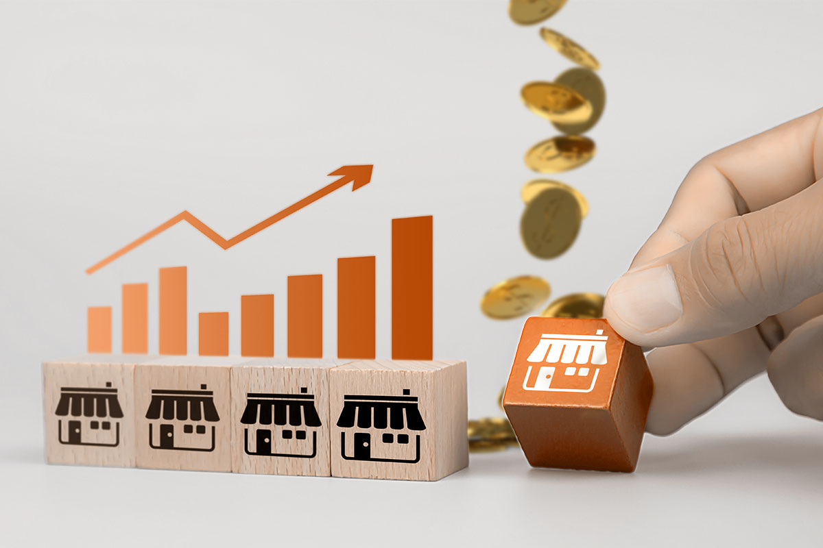 Advantages and Disadvantages of Franchising 1 A row of wooden blocks with store symbols representing franchises with a growth graph and coins in the background.