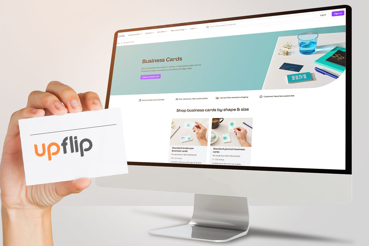 A hand holding an UpFlip business card next to a computer monitor showing a business cards page on Canva.
