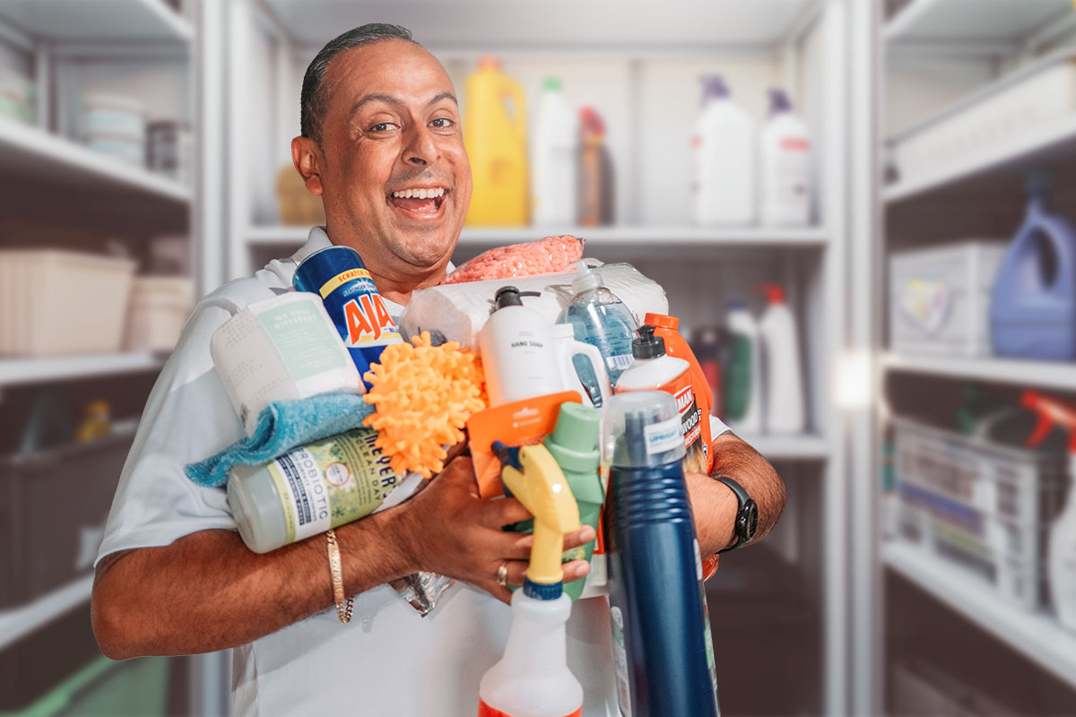 Chris Mondragon in a supply closet holding a variety of different cleaning products.
