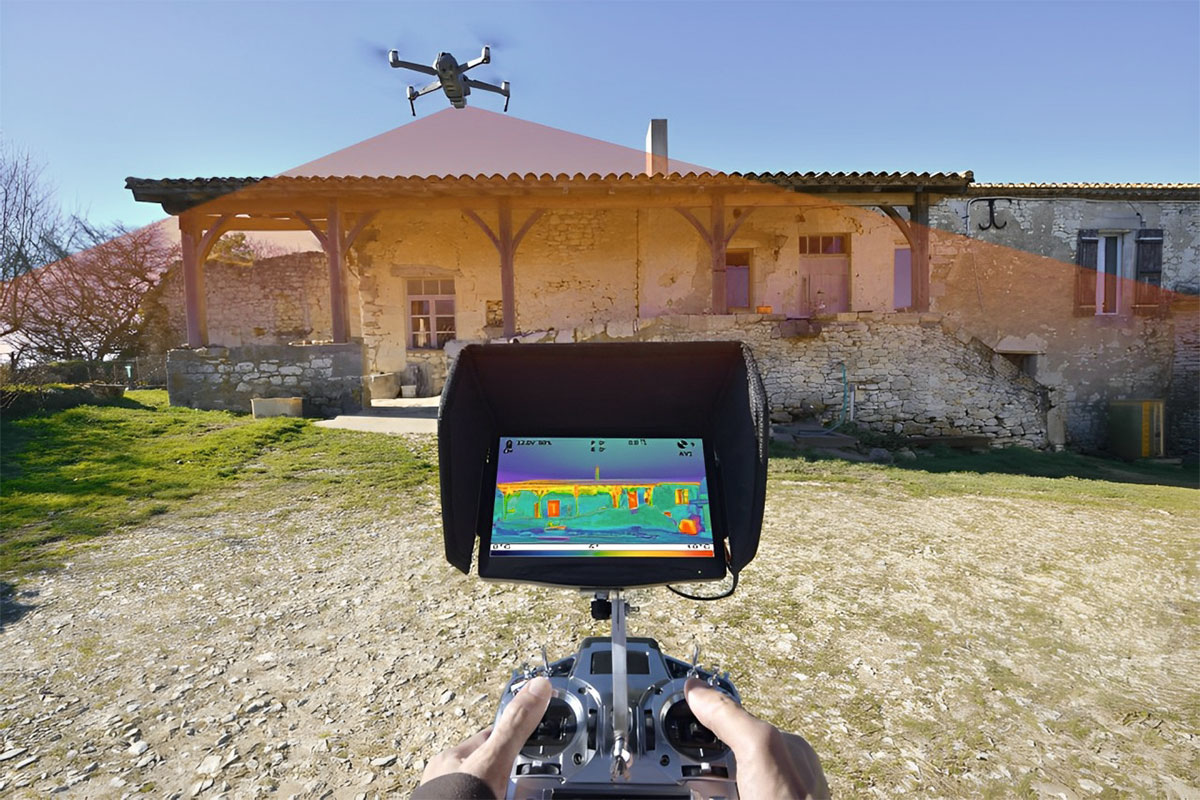 View of a thermal imaging screen in front of a house while a drone flies overhead scanning the building.