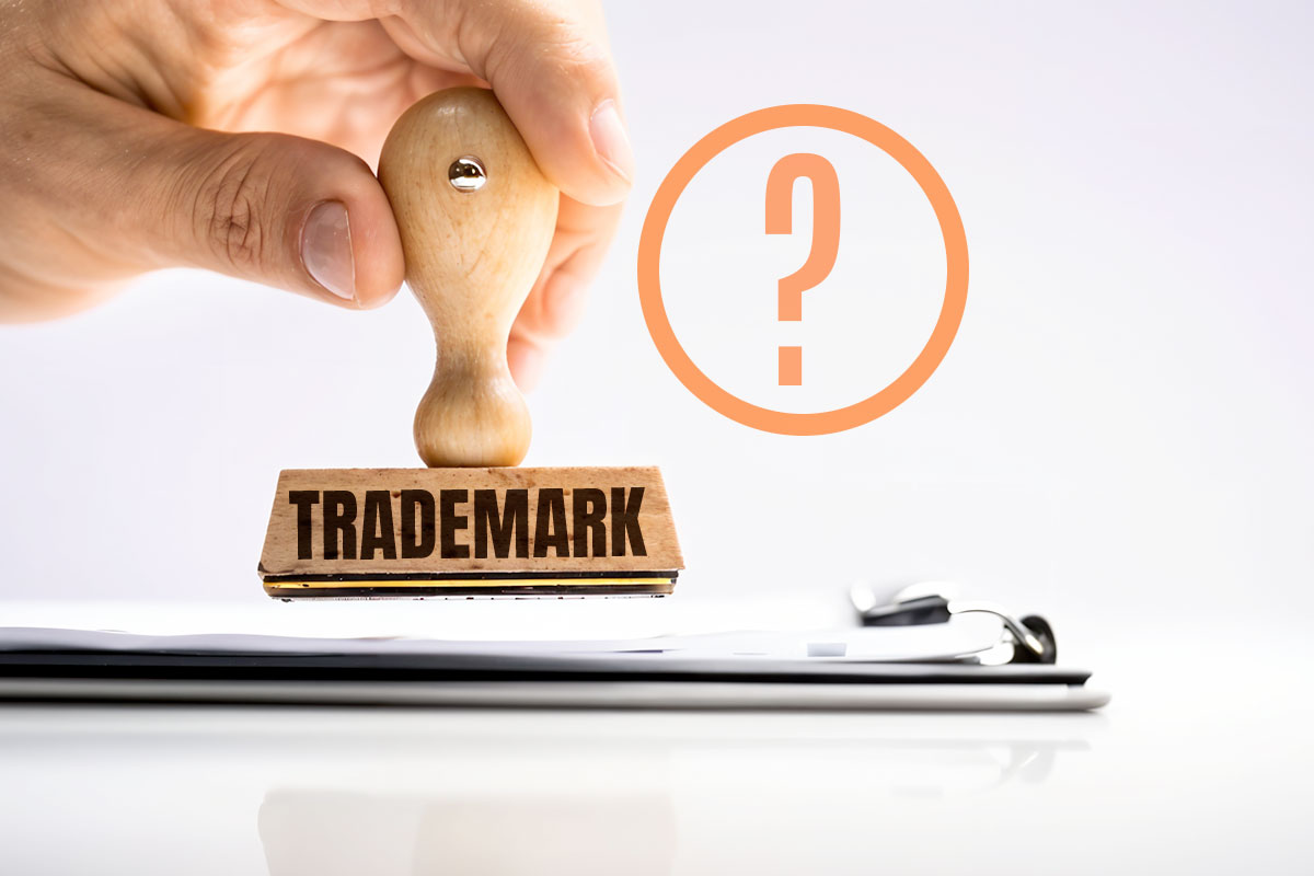 How to Trademark a Name in 5 Steps 1 A person using a wooden ink stamp labeled trademark while a question mark floats overhead.
