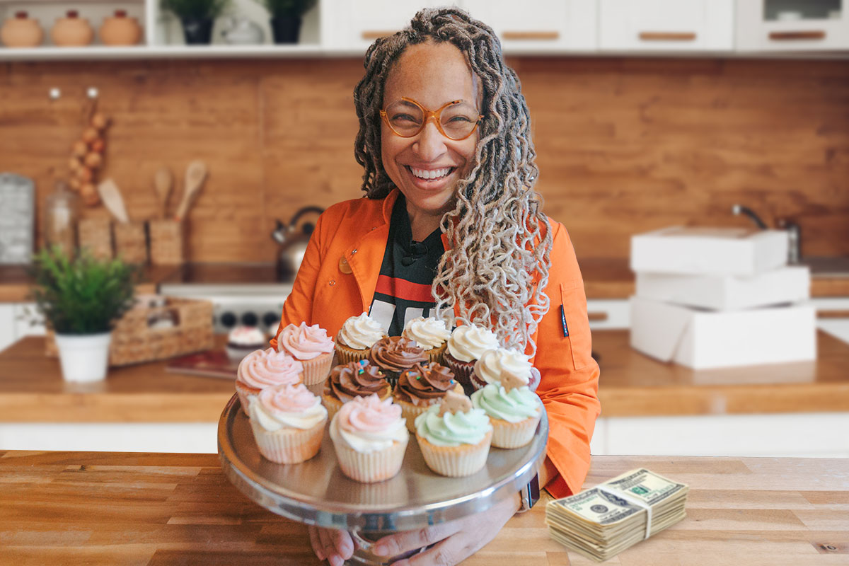 The owner of The Cupcake Collection holding a tray of cupcakes next to a stack of cash on a bakery counter.