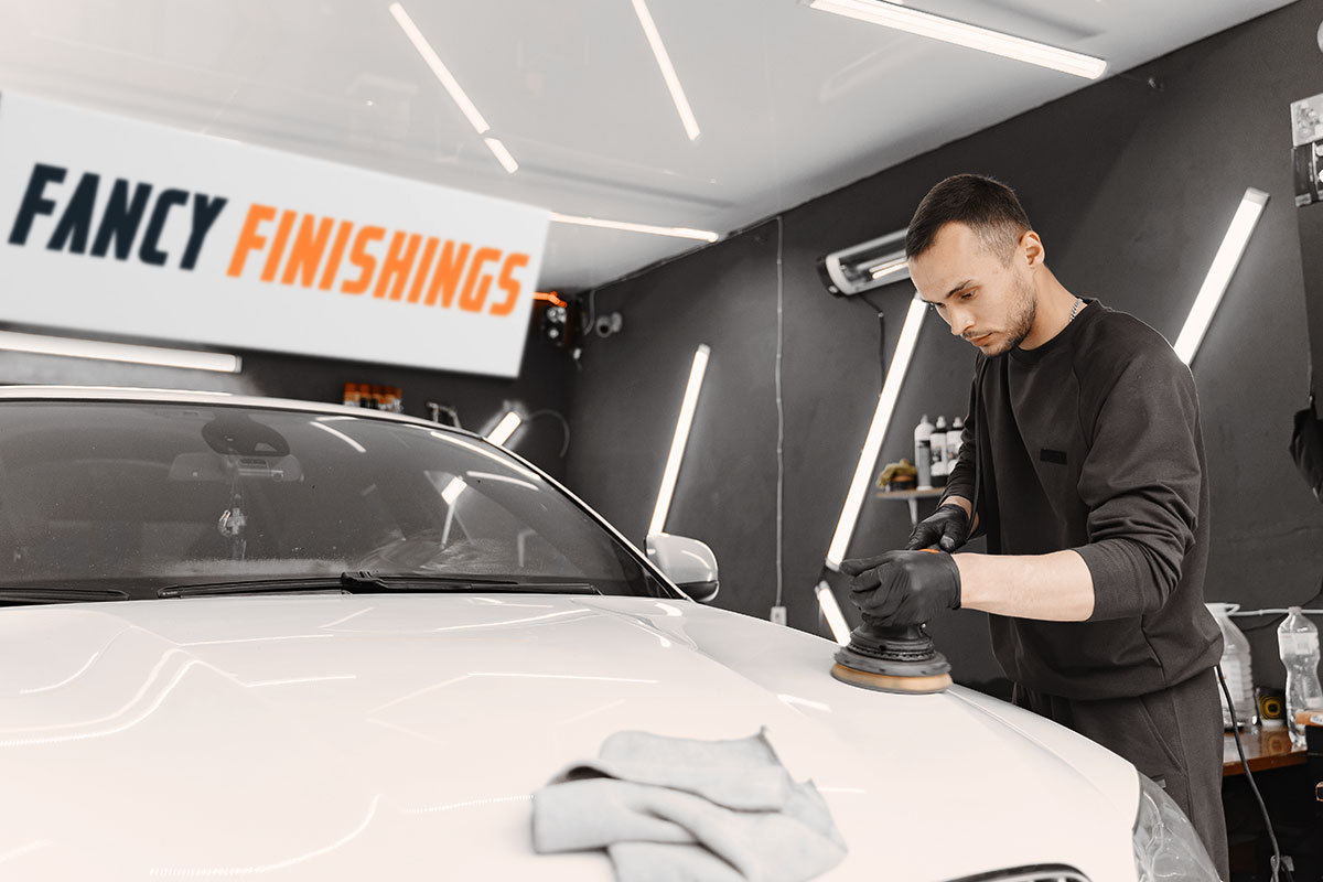 An employee polishing a car inside a shop with a sign that says Fancy Finishings hanging in the background.