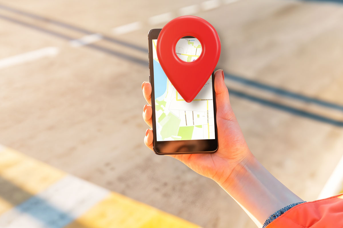 A hand holding a mobile phone with a map locator icon popping out of the screen.